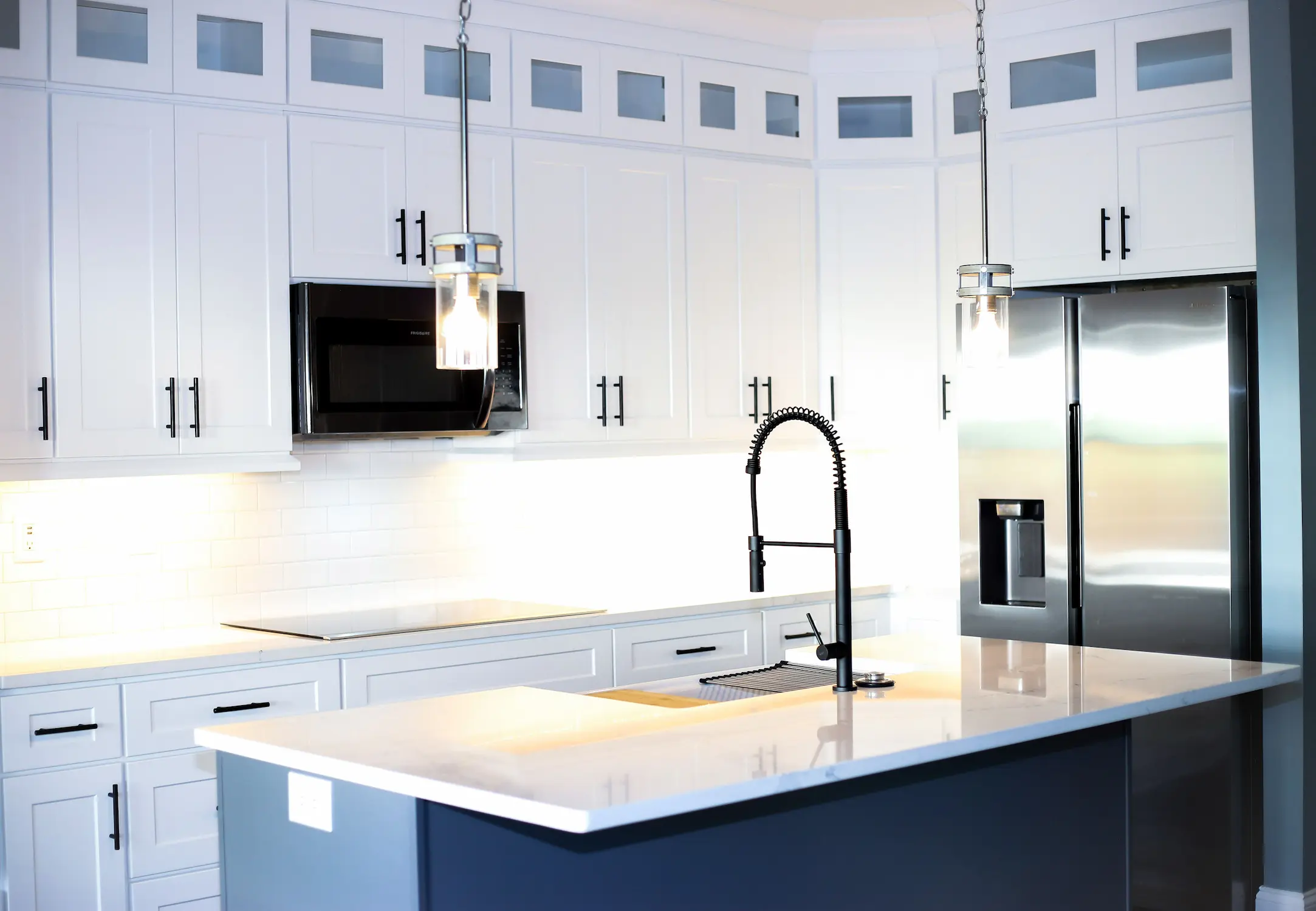 White shaker kitchen with navy island, pendant lights and spring-neck faucet
