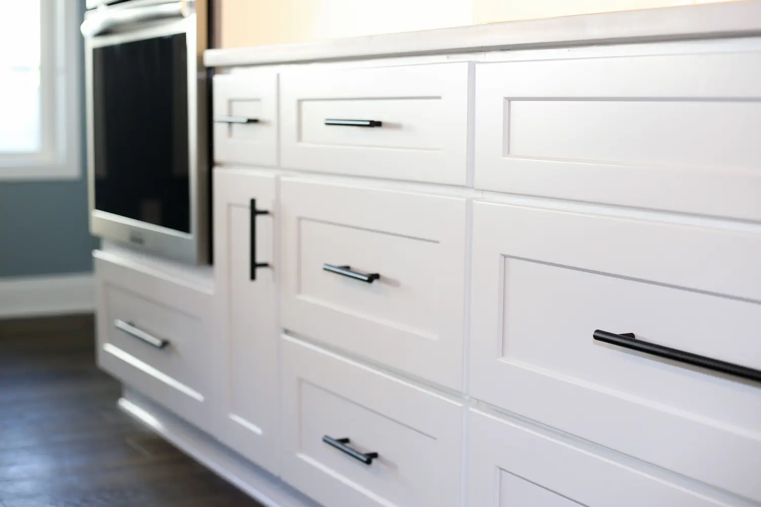 White shaker drawer bank with matte black bar pulls beside a wall oven