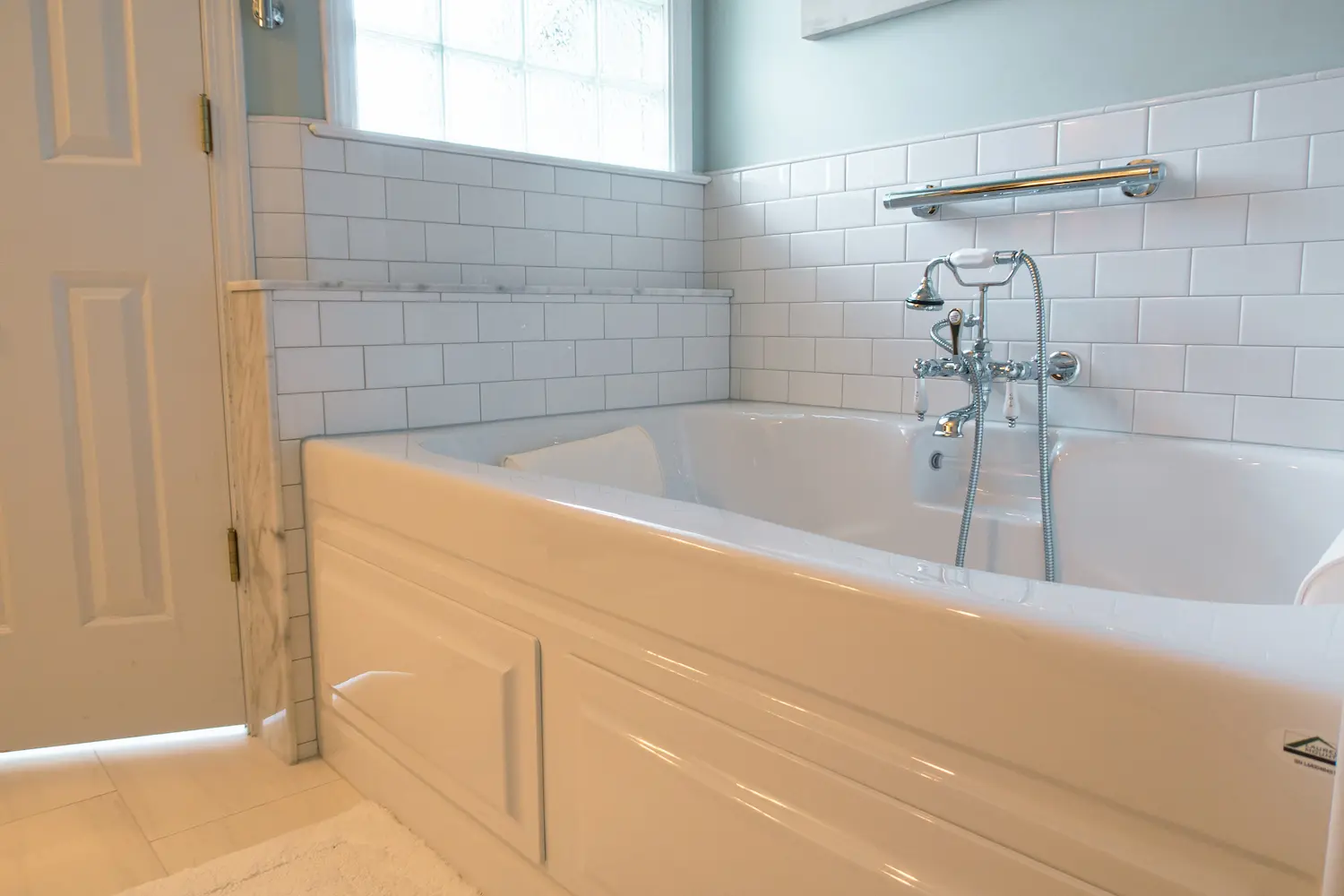 Soaking tub with chrome tub filler against white subway tile