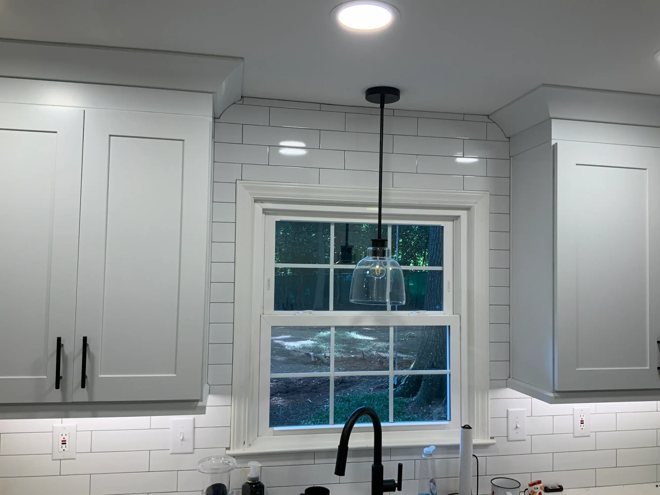 White subway tile and grey cabinets framing a kitchen window