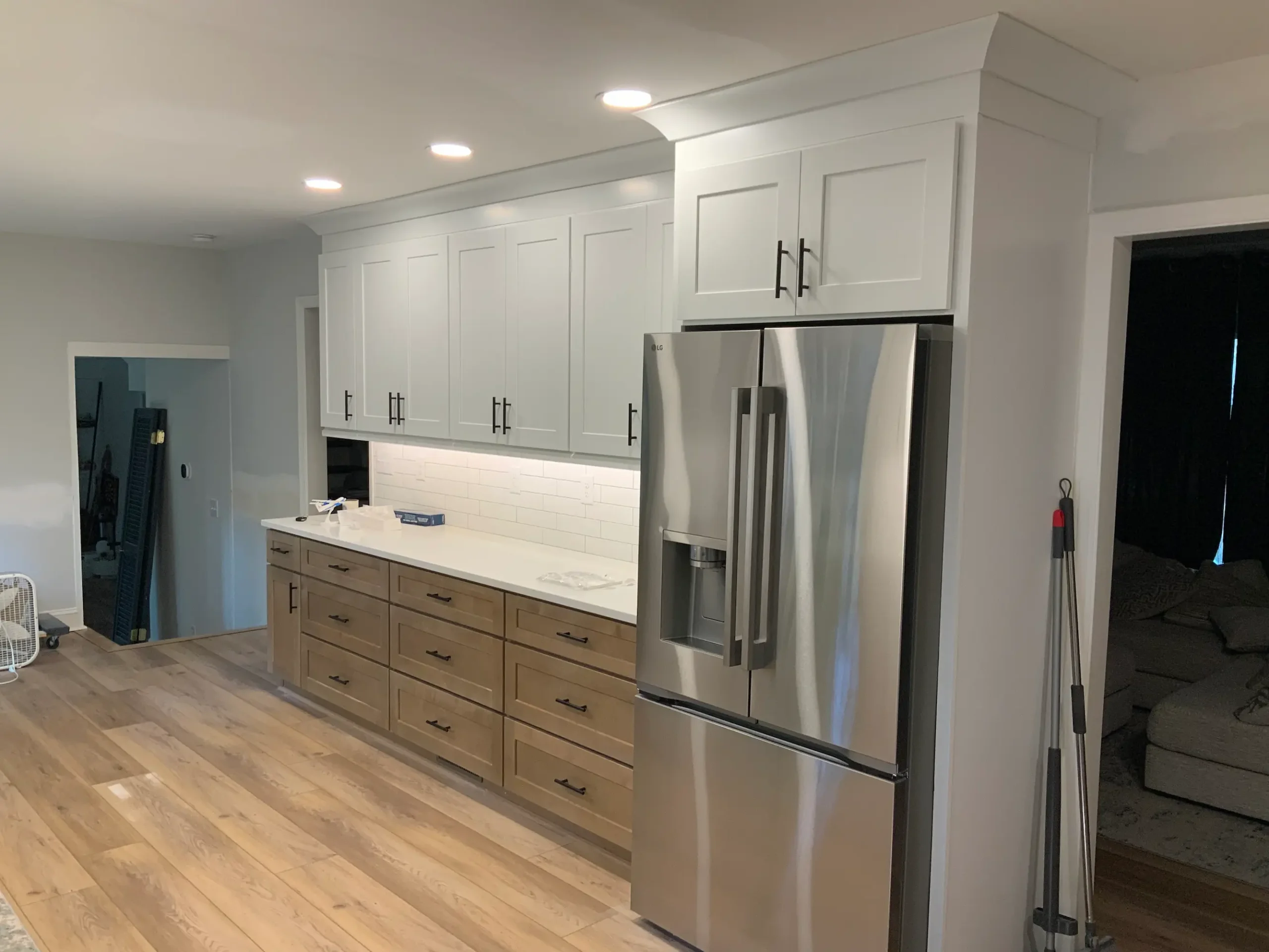 Wood base cabinets and white uppers beside a stainless refrigerator
