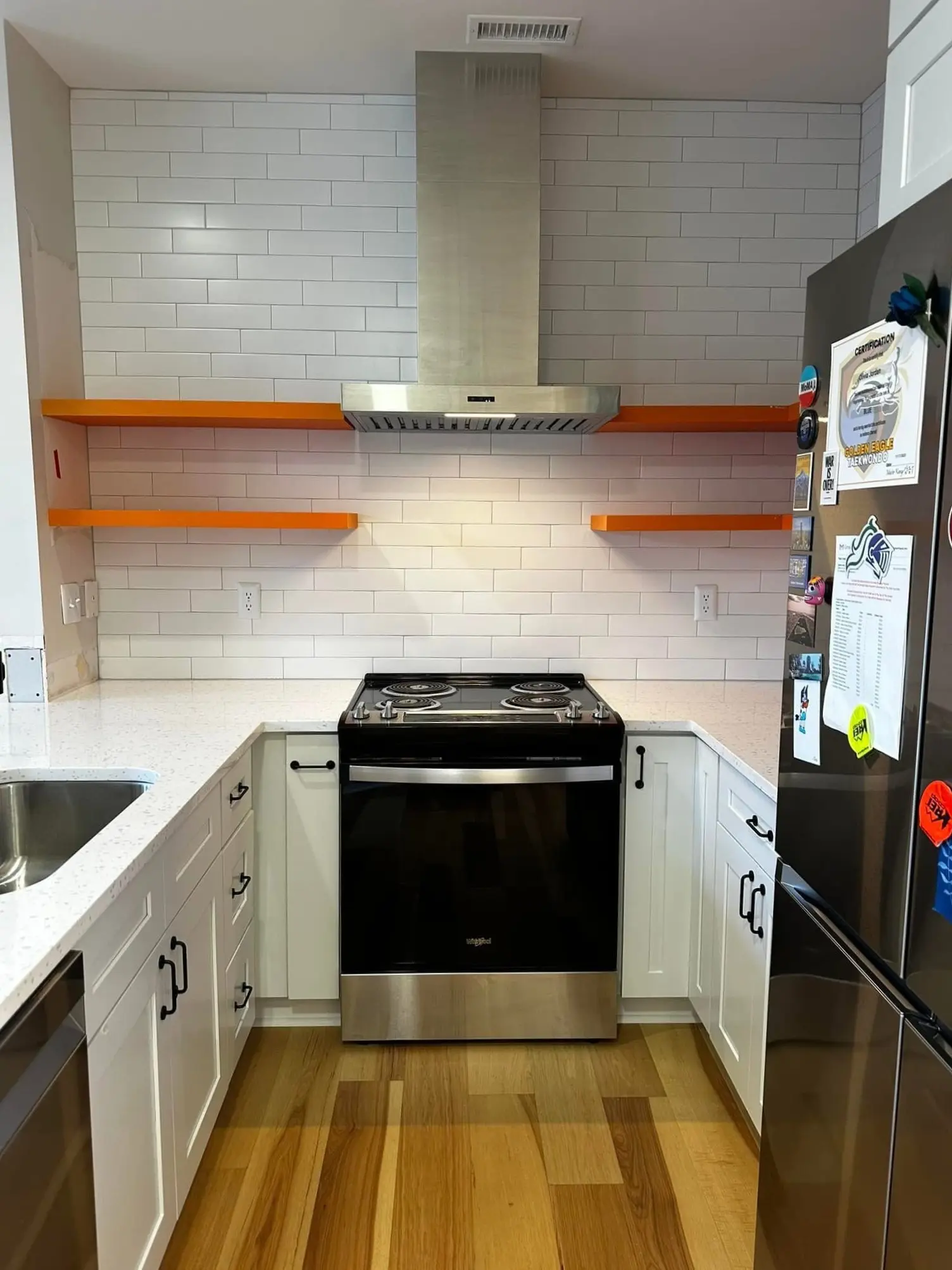 Stainless hood and range flanked by orange floating shelves