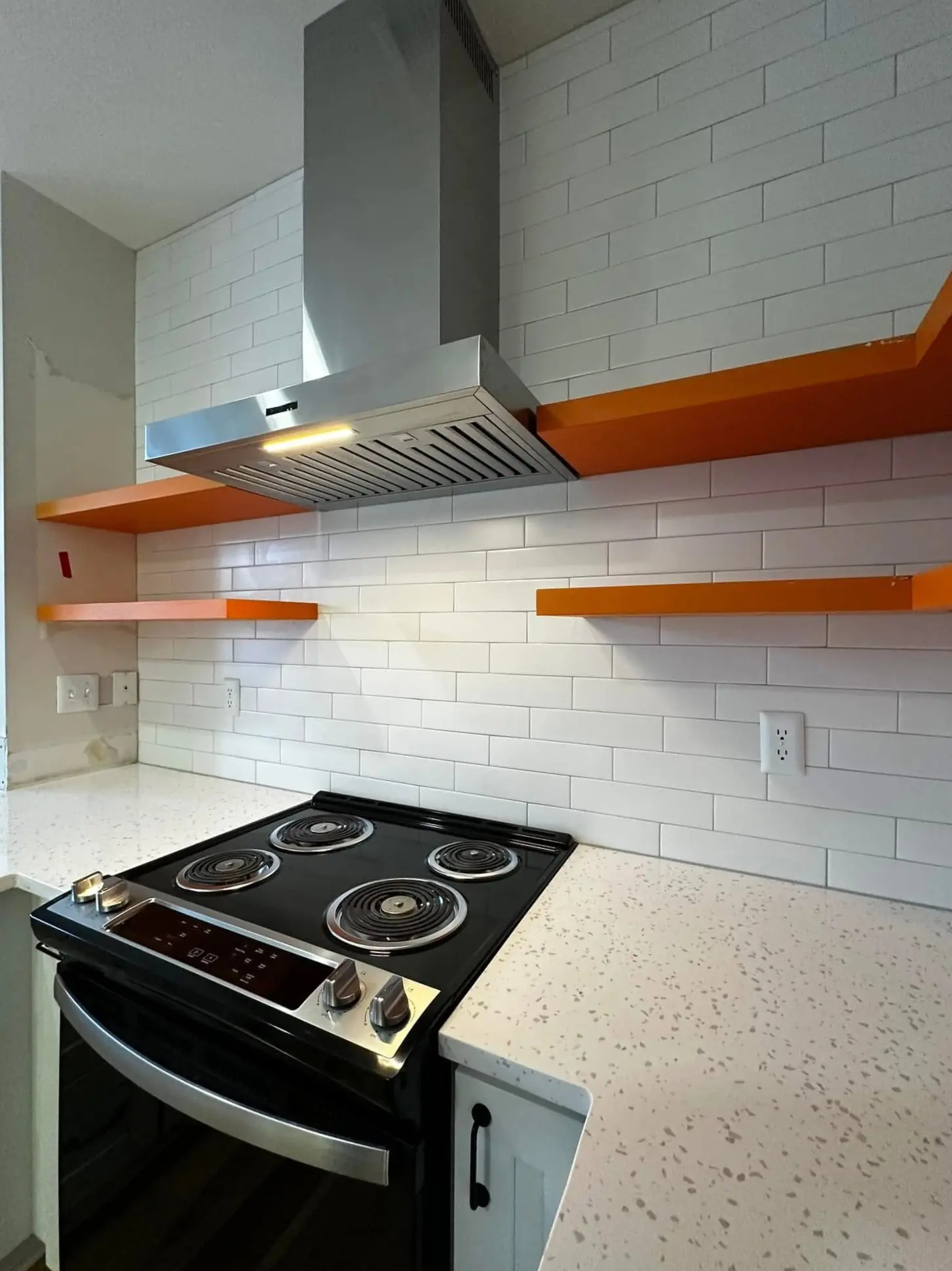 Black electric range below orange shelves on white subway tile