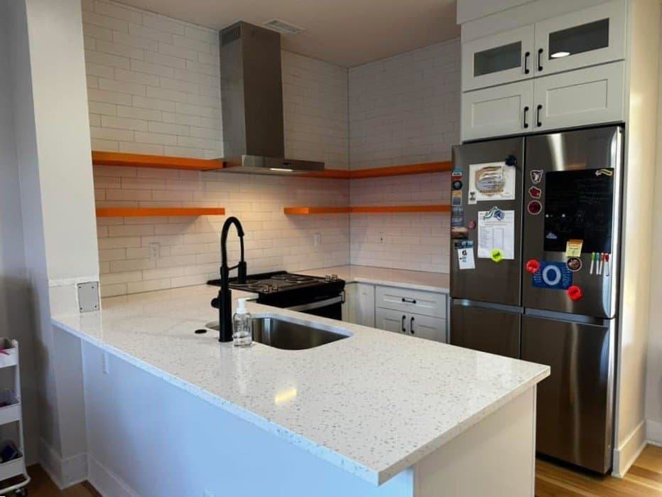 Speckled quartz peninsula with orange floating shelves and vent hood
